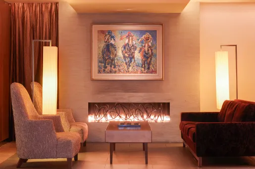 Two cushioned chairs in front of a fireplace with a painting of horse riding above