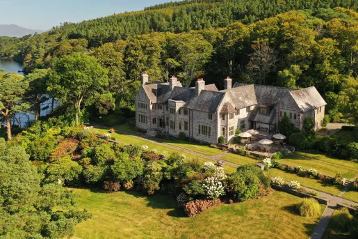 Sky view of stone building with large grass field, surrounded by trees