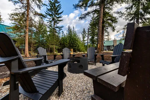 Black reclining chairs surrounding a black fire pit in the middle of a forest