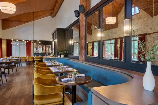 Dining area with a long, gray booth across 4 wooden tables and cushioned chairs on the opposite side