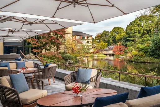 Outdoor balcony with cushioned chairs, looking out to a small lake and forest