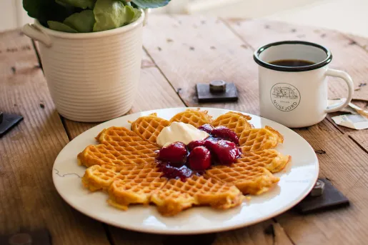Plate of a waffle with butter and jellied fruit, with a cup of coffee on the right