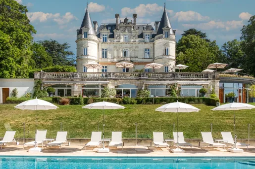 Outdoor pool with white chairs surrounding it, with a castle-like building in the distance