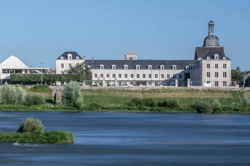Wide, exterior view of a long hotel building behind a small lake