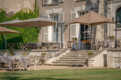 Outdoor patio area with white metal chais, brown umbrellas and a stone building on the right