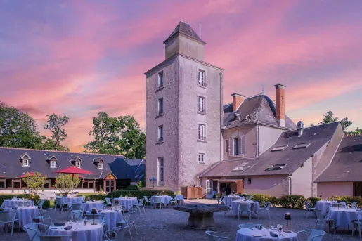 Outdoor couryard filled with dining tables and chairs, with stone buildings in the background