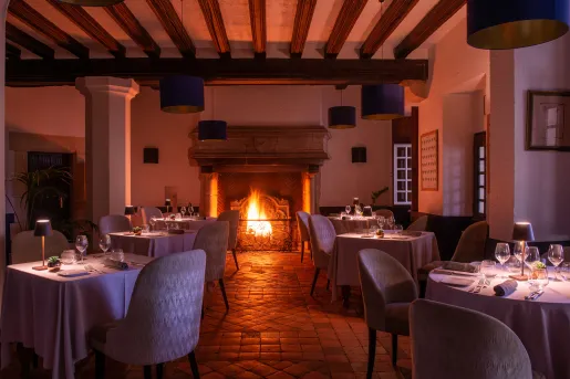 Indoor dining hall with small lamps on each table, and a fireplace in the back