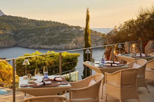 Outdoor patio with woven chairs and glass tables, looking out to a lake