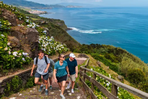# men and 1 woman walking up a flight of stairs on a dirt path sitting on top of a cliff