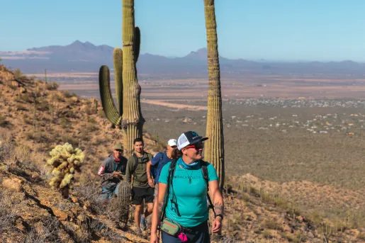 Group of people hiking a dirt trail with two large cacti behind them