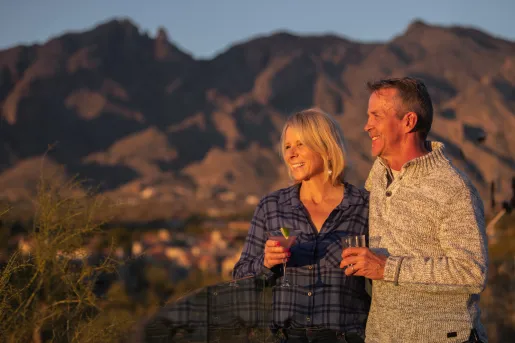 Man and woman smiling while holding martini glasses, looking out to large canyons