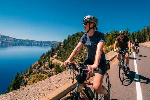 Group of people biking on a road, looking to the left towards a large lake