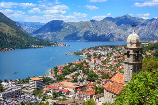 Aerial view of buildings all along the shore of a body of water, mountains in the distance