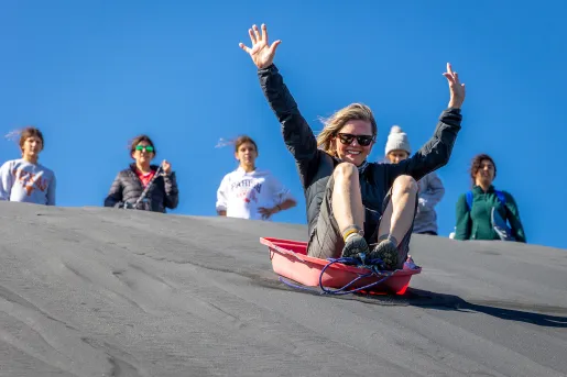 Woman on a red sled, sliding down a sandy hill