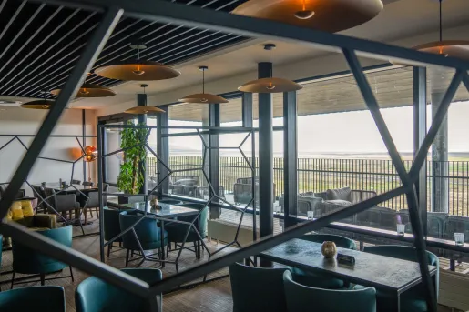 Indoor dining area with stone tables and green, cushioned chairs with large windows