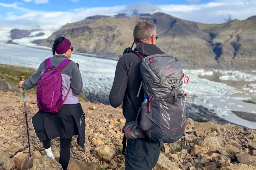 Man and woman hiking on a rock-filled path with a frozen lake to the right