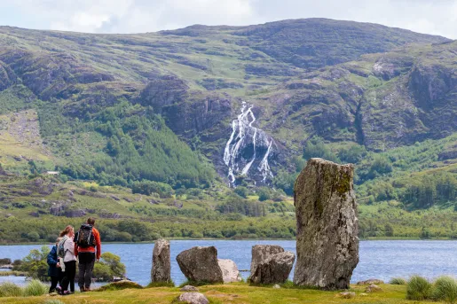 Group of people walking next to a lake with large tree stumps on the right