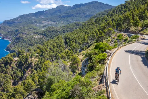 Man biking on a road along a cliff covered with trees