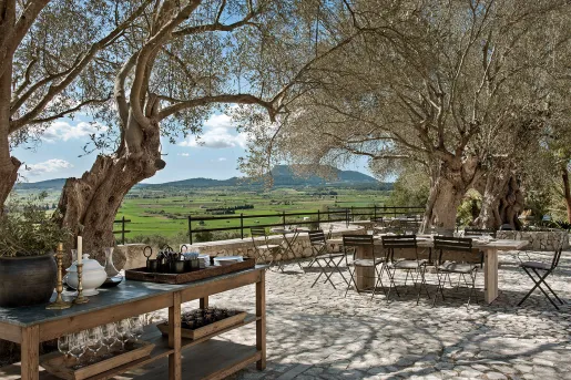 Outdoor seating area with wooden chairs and tables, with a large grass valley in the background