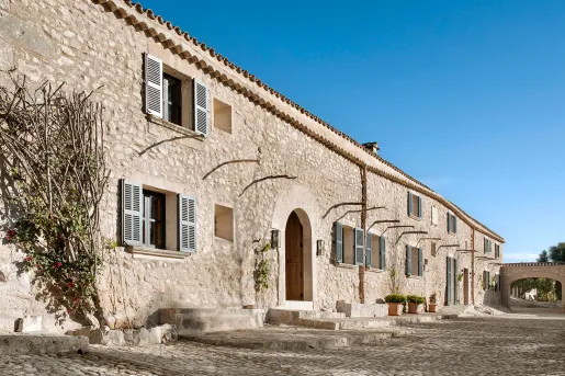 Long, stone building with a stone pathway and branches along the wall