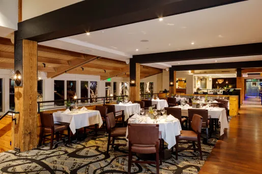 Indoor dining area with large black pillars, and leather chairs around white dining tables