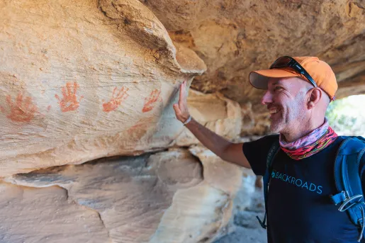 A man holds his hand up to handprints on a stone wall