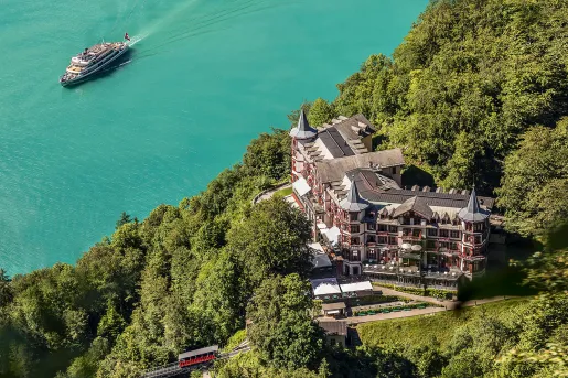 Sky view of  castle-like hotel building surrounded by trees and a cruise boat in the ocean on the left