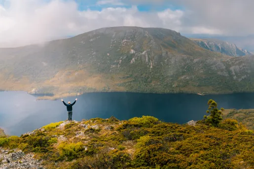 Man with his arms open while standing on a cliff, looking out to a large lake