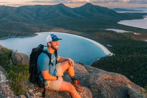 Man smiling while wearing a backpack on top of a large cliff