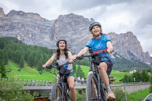 Two women smiling and riding bikes, while looking up to the sky