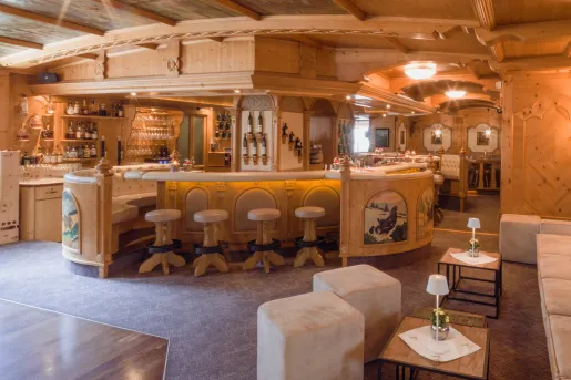 Bar in the center of a lounge with white stools and bottles of wine on the walls