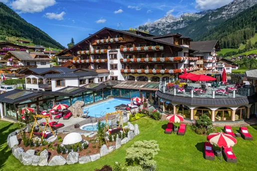 Outdoor courtyard of a large hotel with balconies, and an outdoor pool with tables and chairs surrounding