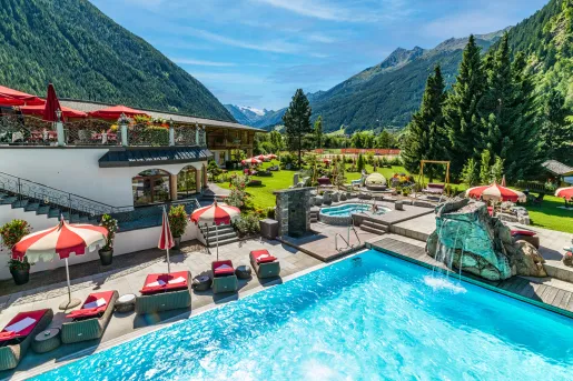 Outdoor pool with a rock fountain and red umbrellas and chairs surrounding it