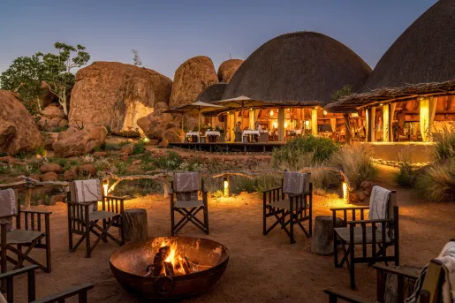 Woven chairs surrounding a fire pit, with straw huts in the background