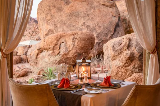 Dining table with wine glasses and a lantern with giant boulders in the background