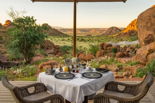 Dining table with woven chairs, looking out towards a large valley
