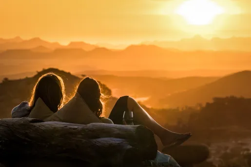 Three women sitting on a bench looking out to an open valley and a sunset