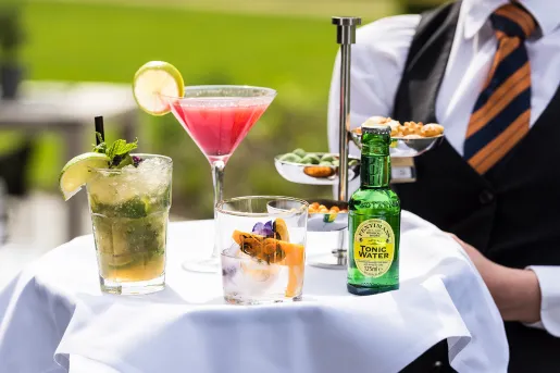 Waiter holding a tray full of mixed drinks and a bottle of tonic water