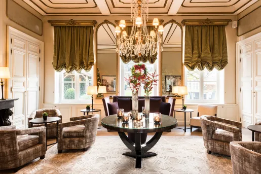 Indoor lounge with cushioned chairs and a large, crystal chandelier on the ceiling
