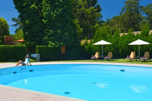 Woman sitting next to a pool, surrounded by green trees