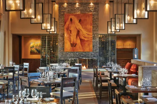 Indoor dining hall with wine glasses on the tables with a large painting of a horse on the wall