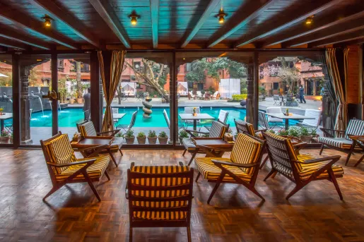 Outdoor patio with cushioned, wooden chairs looking out to an outdoor pool