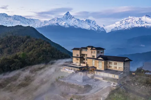 Hotel on top a hill surrounded by fog with mountains in the back