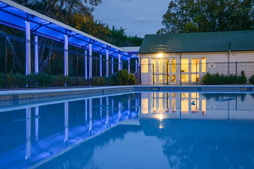 Outdoor pool with a building and covered walkway illuminated by blue and orange lights