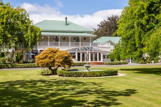 Exterior view of yellow and green building with a grass field and a fountain in the center