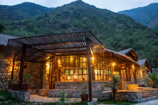 Exterior view of illuminated stone building, with a tall grass mountain in the background
