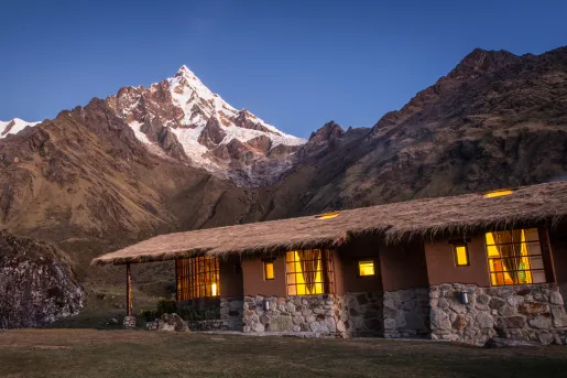 Stone building with a straw roof in the middle of a grass valley, with large mountains in the background