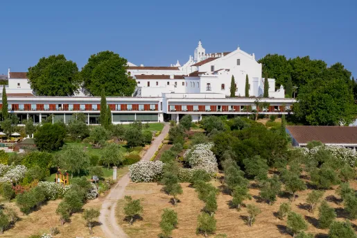 Exterior view of wide, white building with red balconies with a large valley of trees in front