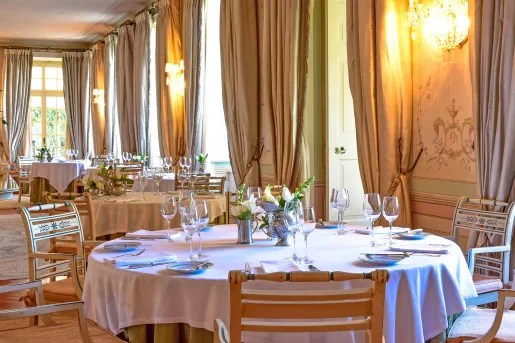 Dining area with large curtains, circular tables, and wine glasses on each table
