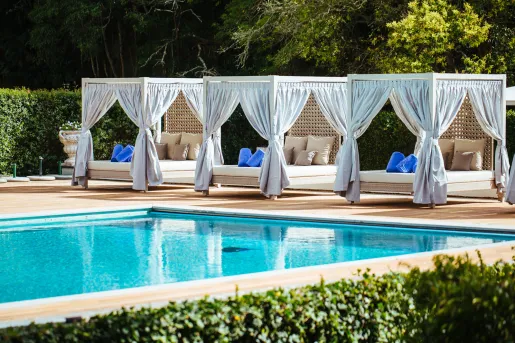 Outdoor pool with beds with large curtains surrounding the pool